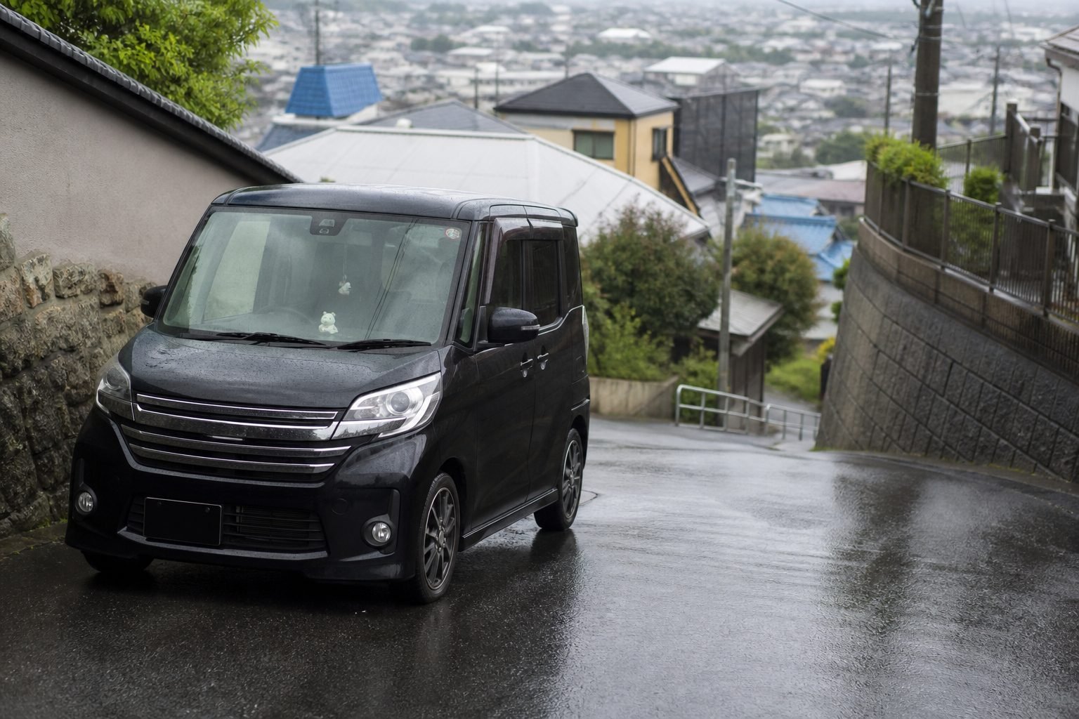 Tall Japanese kei wagon on a steep wet residential street